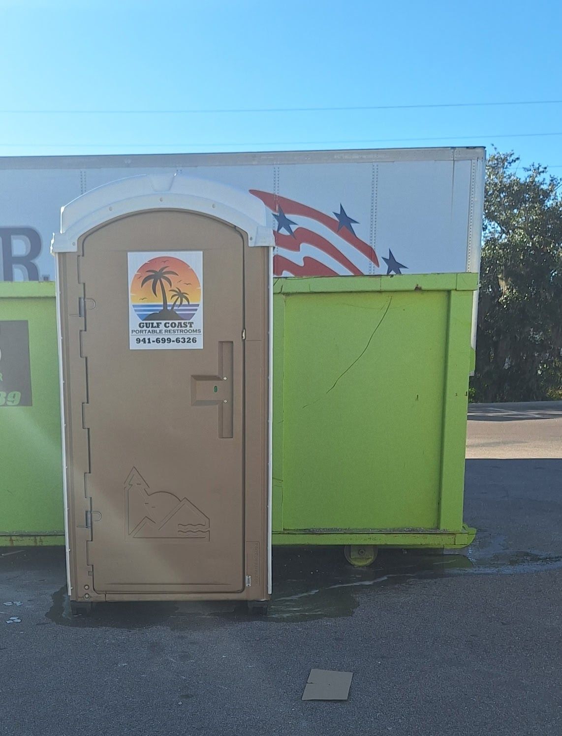 Beige portable toilet in front of a lime-green dumpster and white building with palm logo mural.