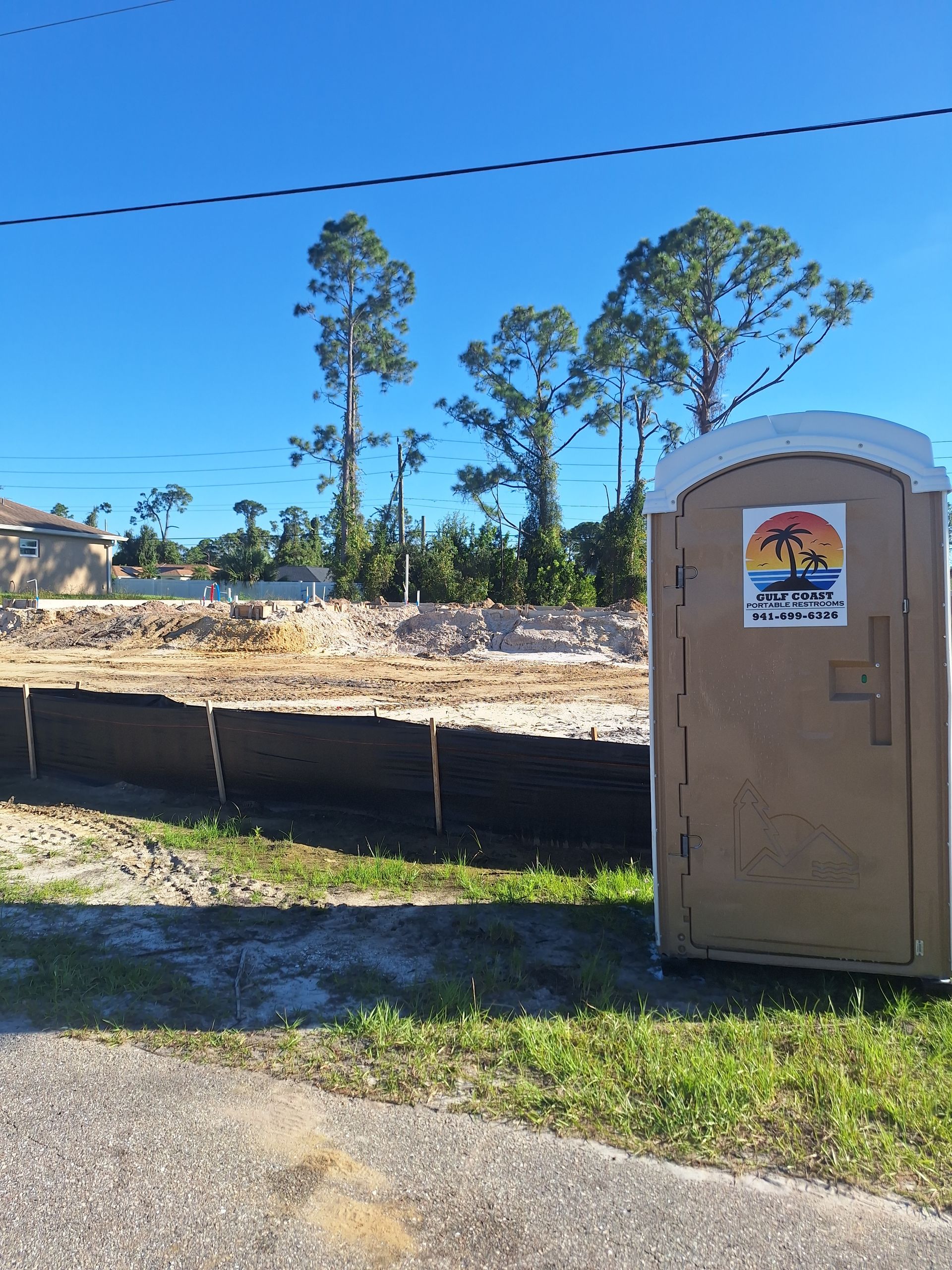 Portable toilet beside a construction site under a clear blue sky