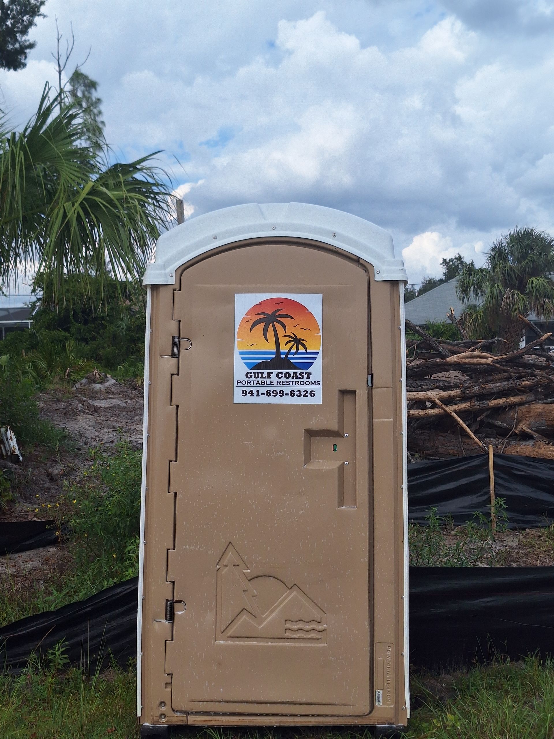 Beige portable toilet on a grassy lot under a cloudy sky, with a beach sign on the door.