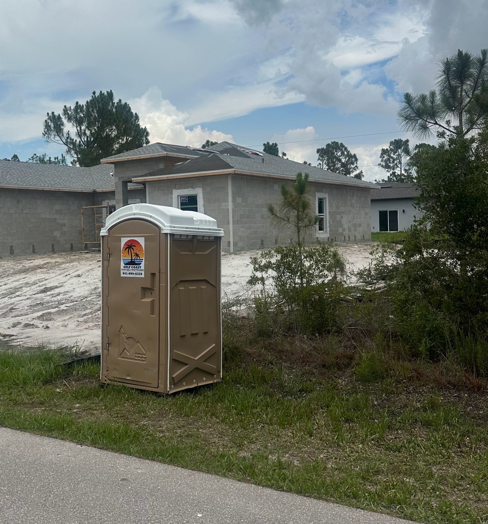 Portable toilet beside a road near an unfinished concrete house under a cloudy sky