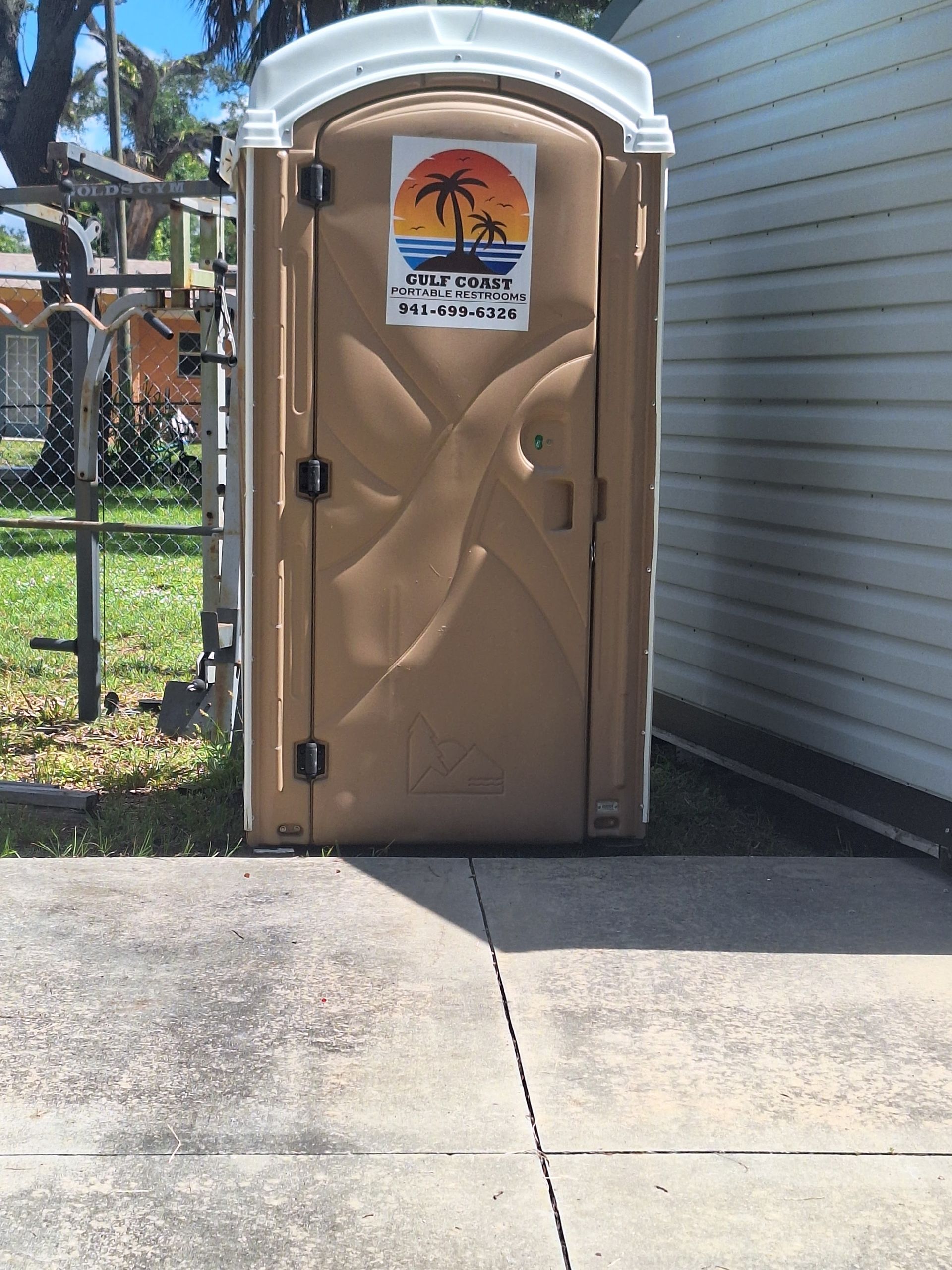 Portable beige restroom beside a building, with a sun logo sign on the door