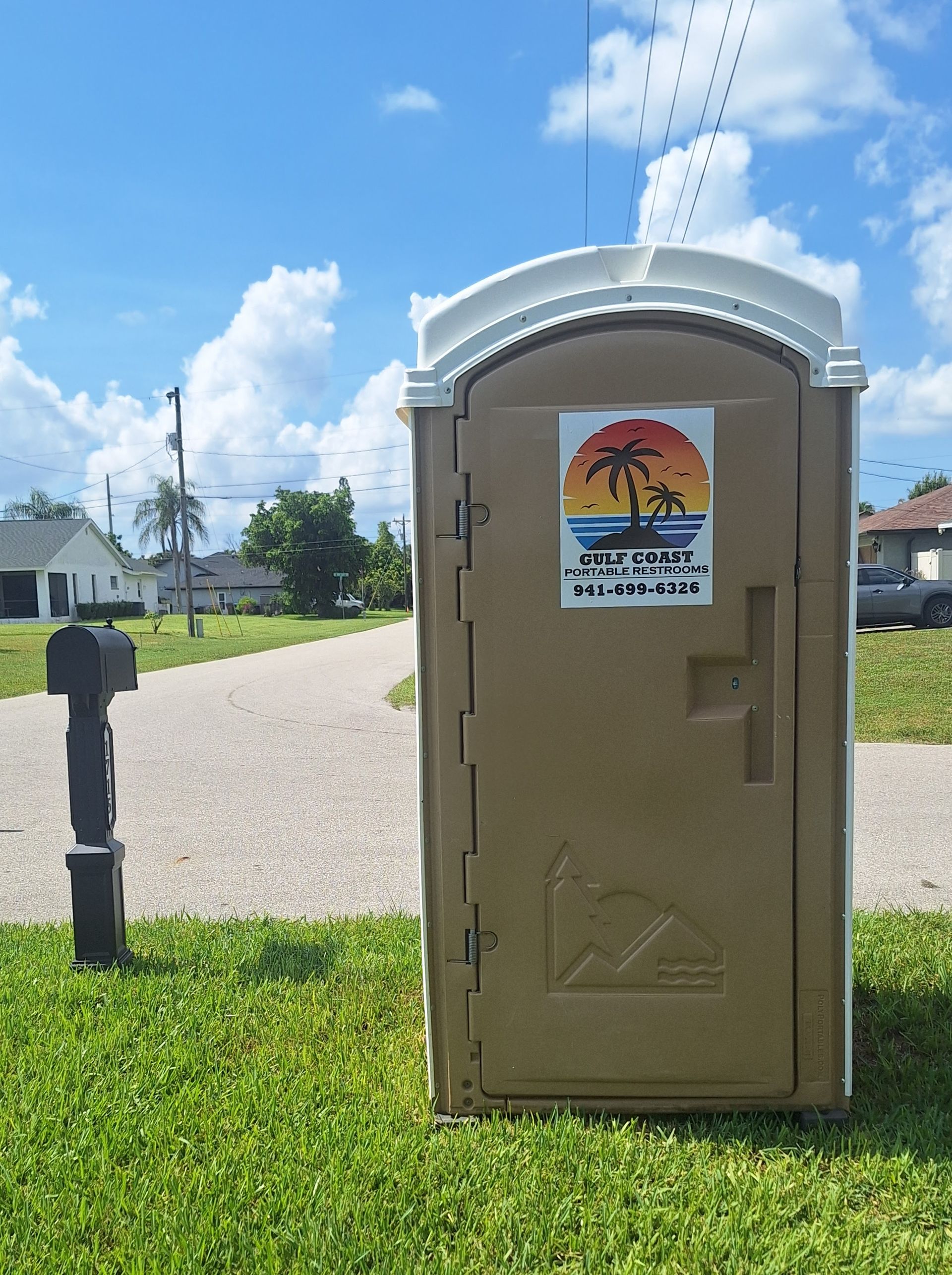 Portable toilet beside a gravel path under a blue sky with clouds, with a warning sign on the door