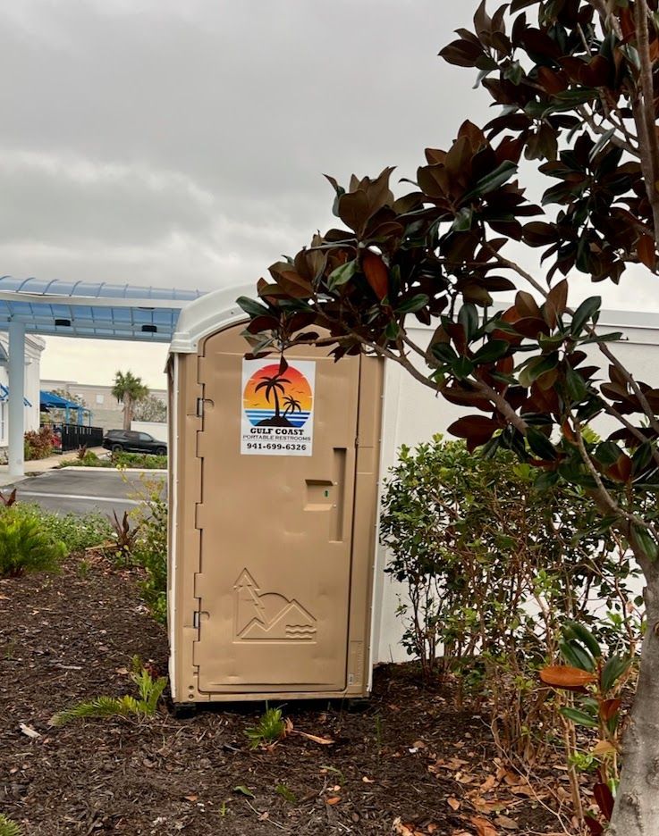 Beige utility box by a road, with a tree branch in the foreground and cloudy sky behind.