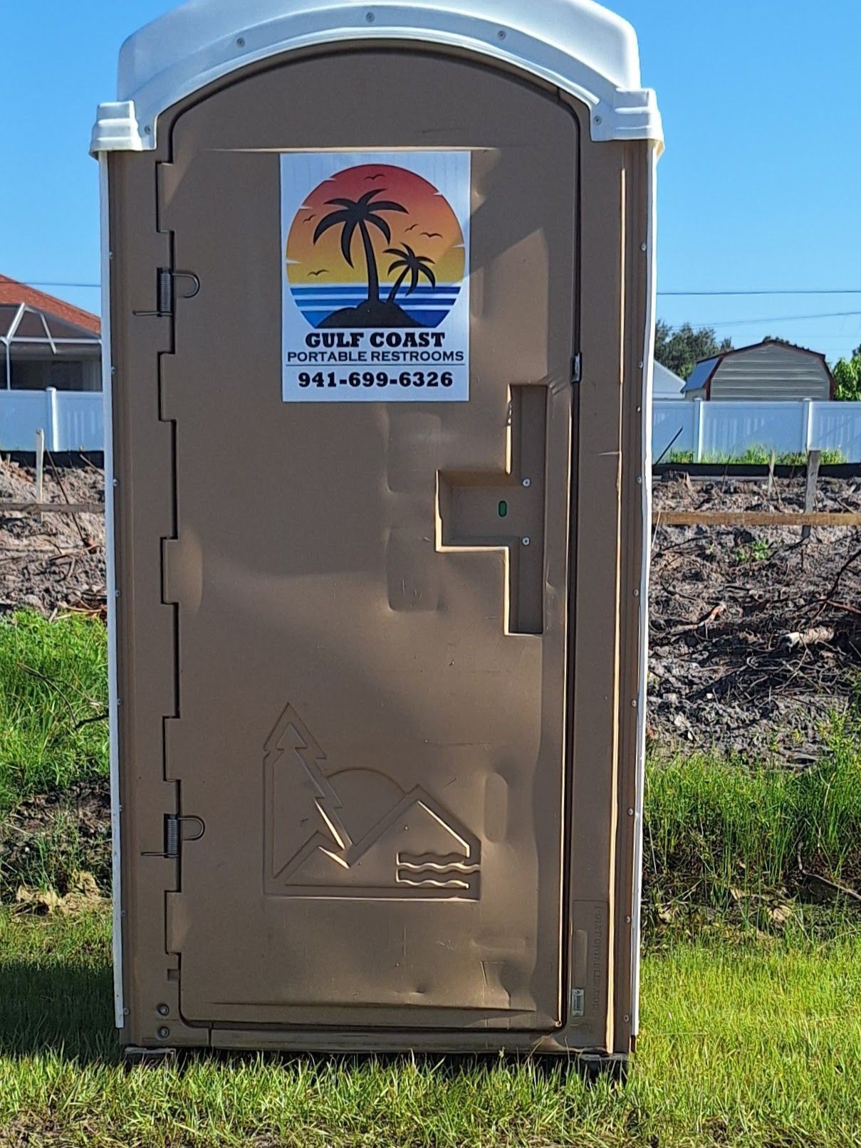 Portable toilet in a dirt lot with a “C.L. Cox” sign on the door, under a clear sky.