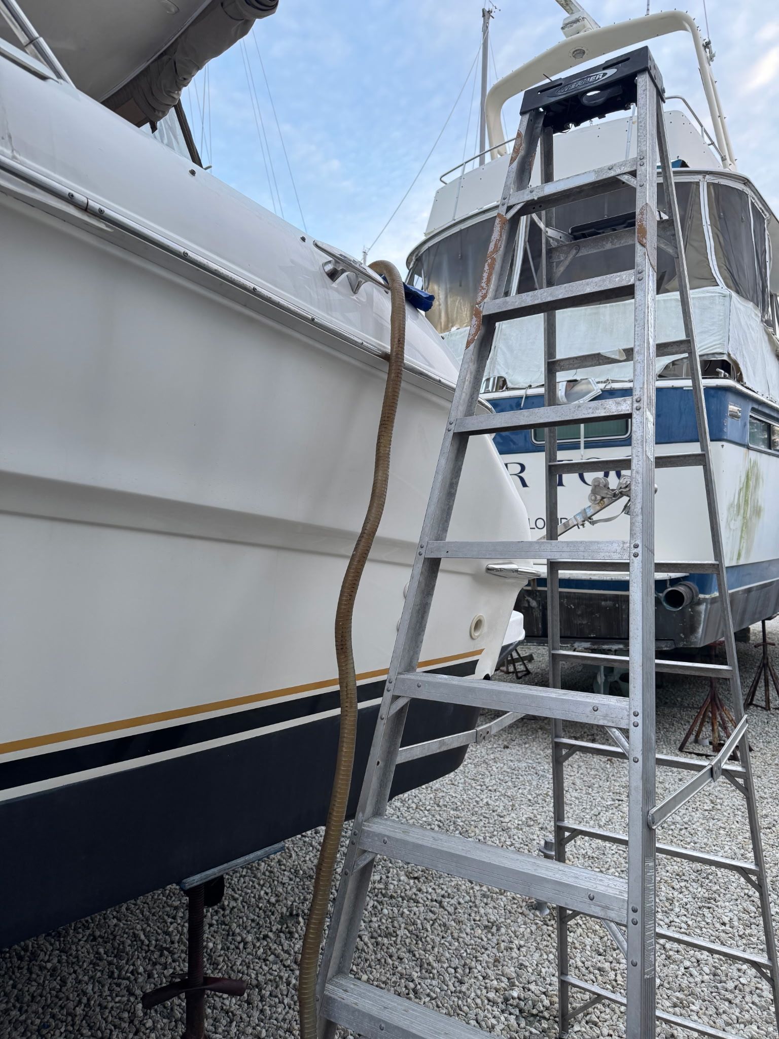 A metal ladder leaning against a boat beside a white dock wall.