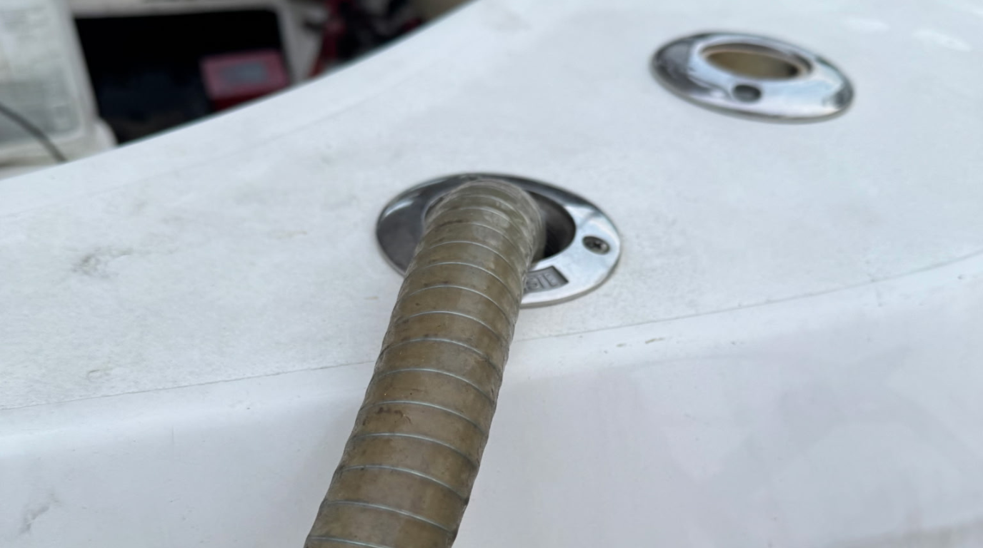 Coiled hose inserted into a white boat deck fitting with a chrome drain or port nearby