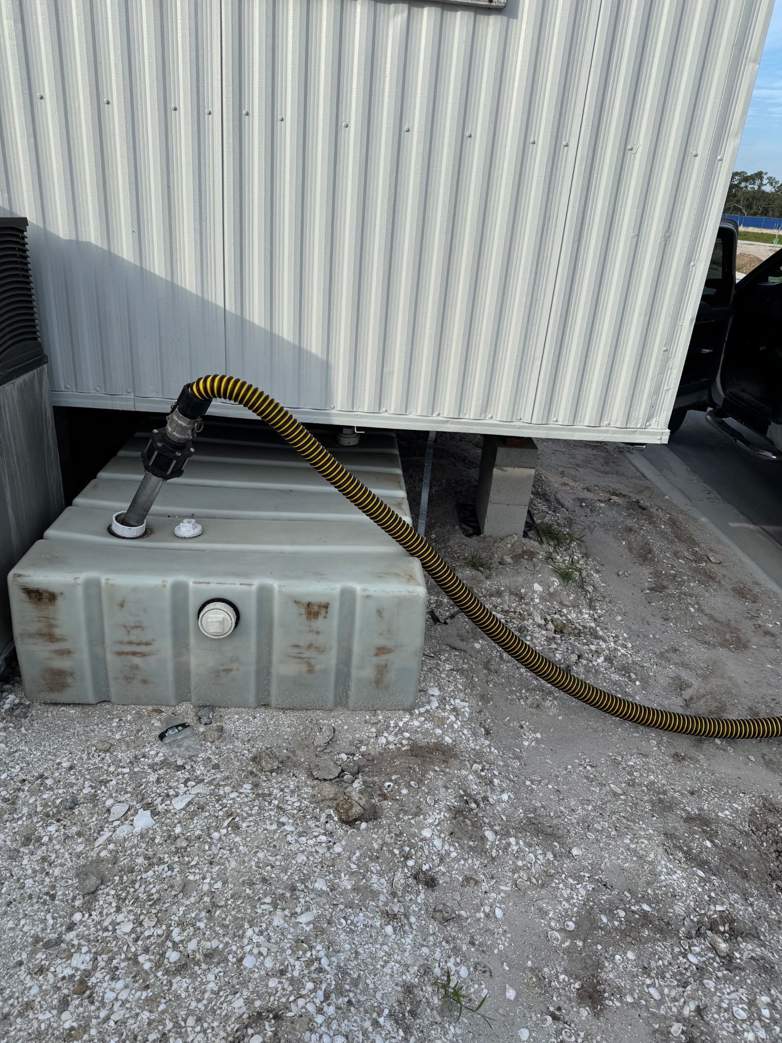 Coiled cable connected to a gray electrical box beside a corrugated metal wall on gravel.