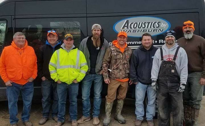 Group of men stand in front of a van with "Acoustics Washburn" logo. Some wear orange hunting gear.