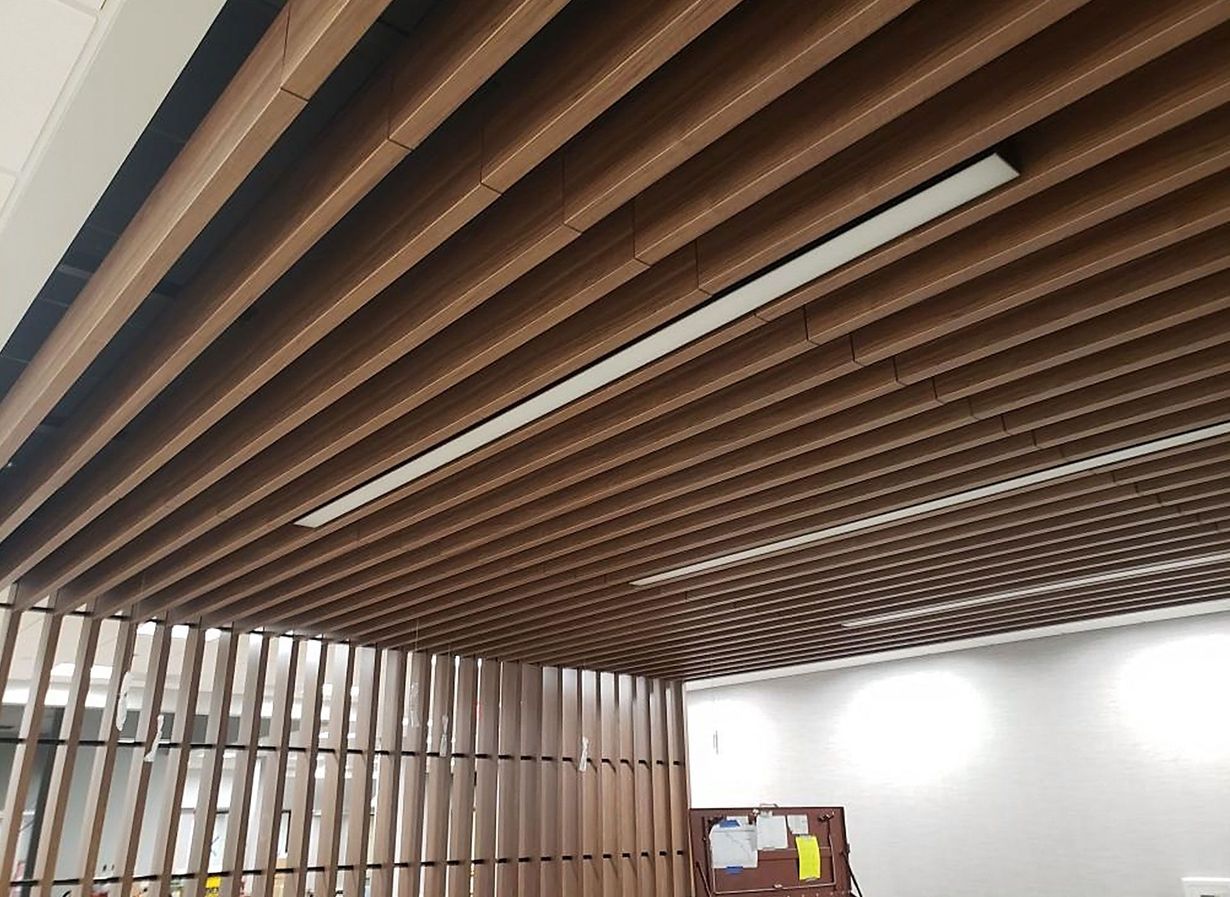 Wooden slatted ceiling with recessed fluorescent lights. Interior view with a partial wooden divider in the foreground.