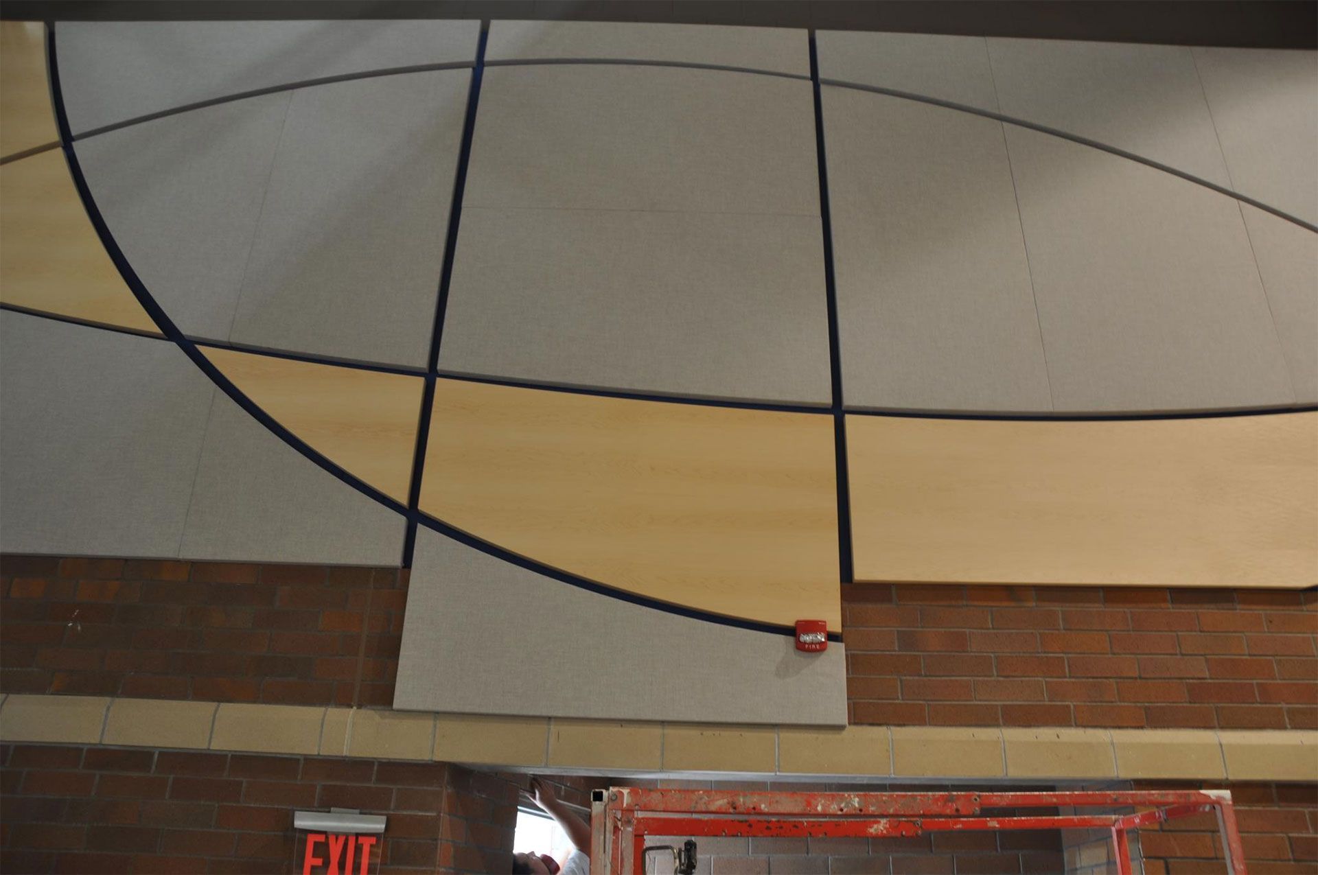 Mural on wall with intersecting lines and rectangles of tan, gray, and black. Brick wall below.