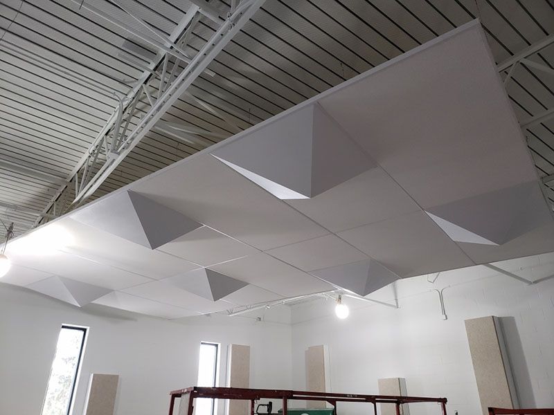 White geometric acoustic panels suspended from a warehouse ceiling.