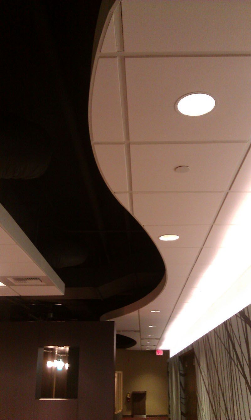 Curving black and white ceiling design with recessed lighting in a hallway.