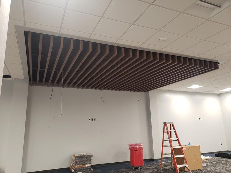 Interior of a room with a suspended wooden beam ceiling. White walls, a ladder, and a red trash can are visible.