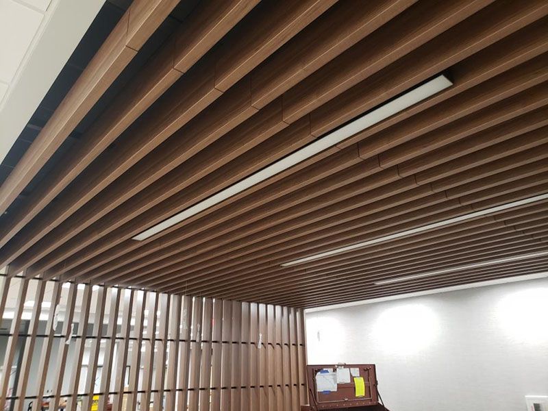 Brown slat ceiling with recessed lighting above a partially visible office space.