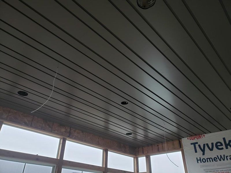 Gray plank ceiling in a room under construction with two recessed lights and windows along the bottom edge.