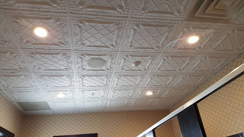 White decorative ceiling with recessed lights, ventilation, and a wall of patterned wallpaper.