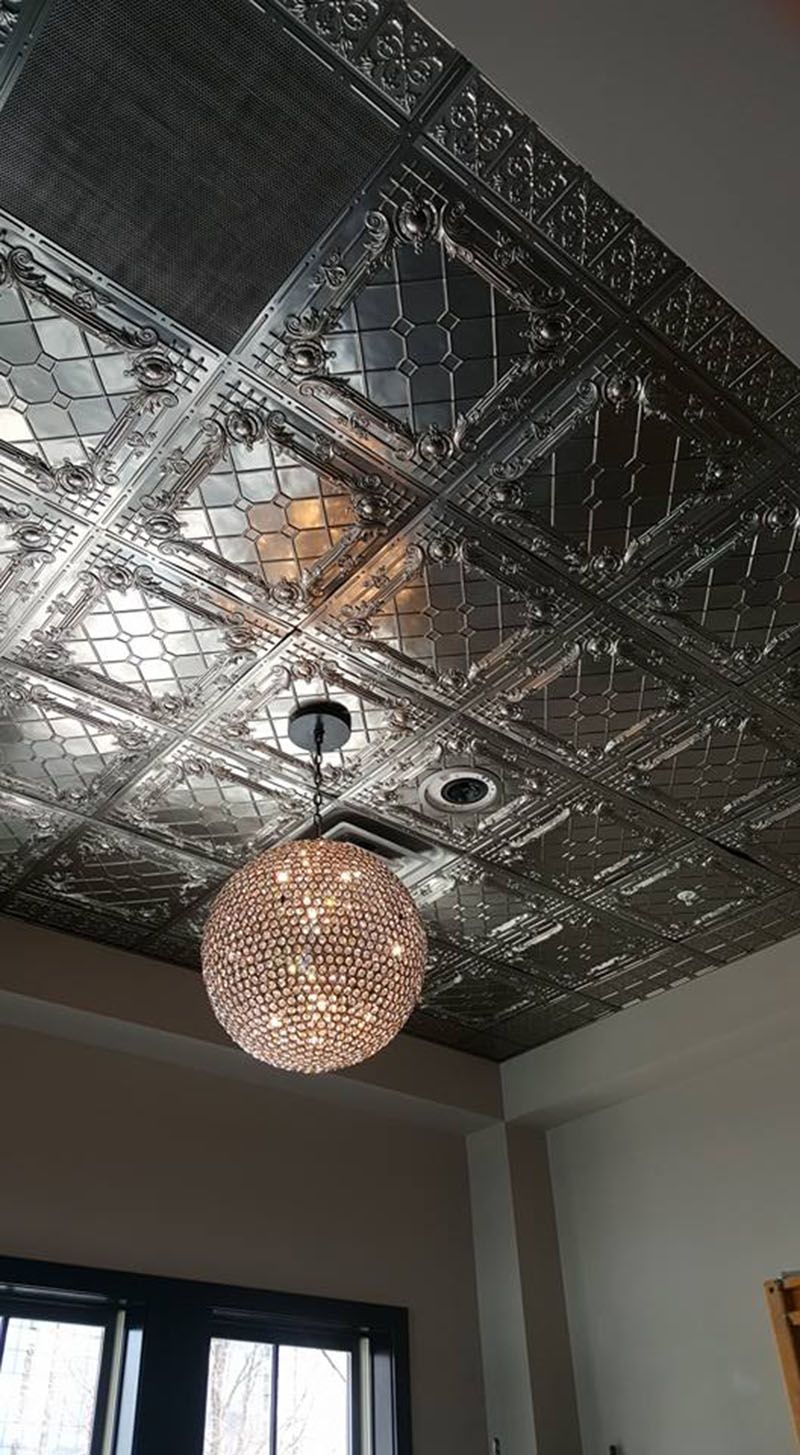 Decorative metal ceiling with a globe-shaped chandelier hanging below, in a room with a window.