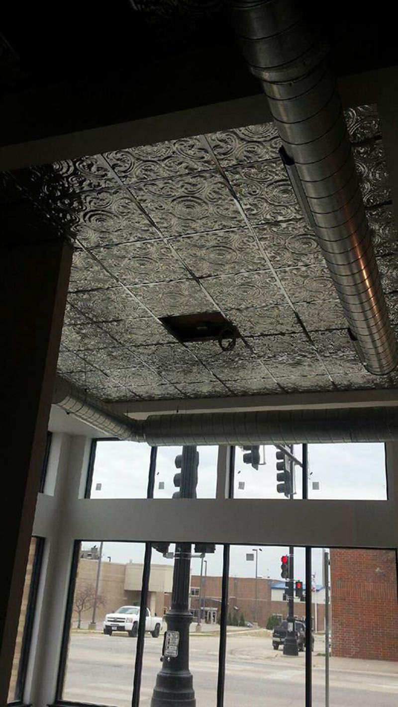 Ceiling with square tiles, a ventilation duct, and a view of a street with traffic lights through a window.