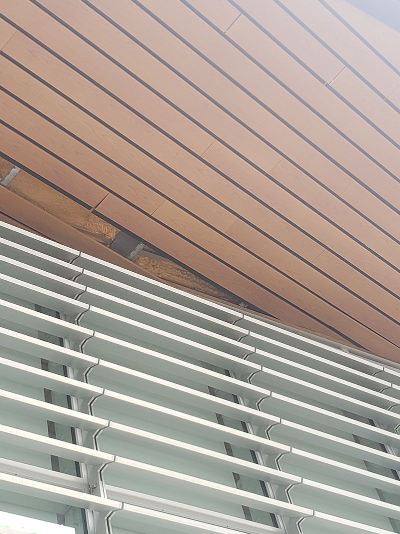 Angled view of a wood-paneled ceiling above horizontal, metal blinds.