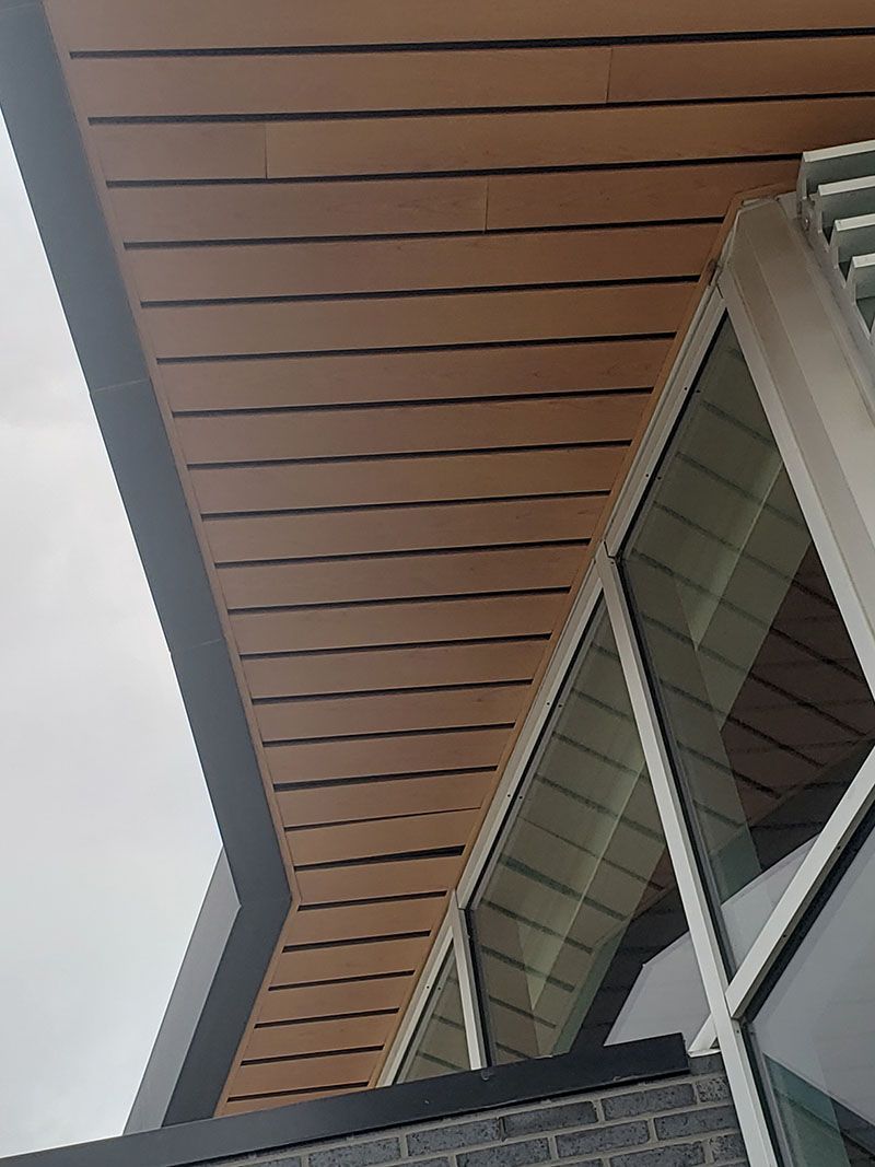 Tan, slatted wood ceiling extending over windows of a building.