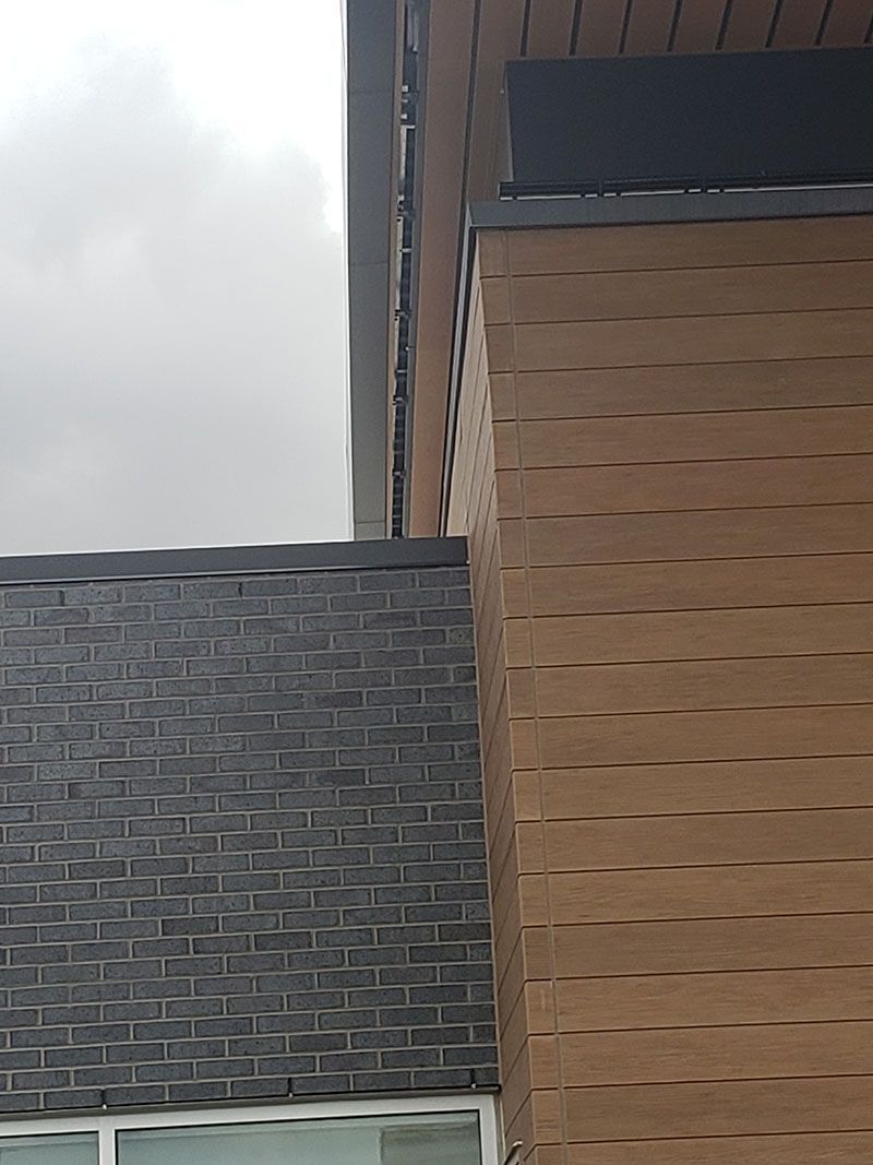 Brown and gray building exterior with shingled roof, brown siding, and cloudy sky.