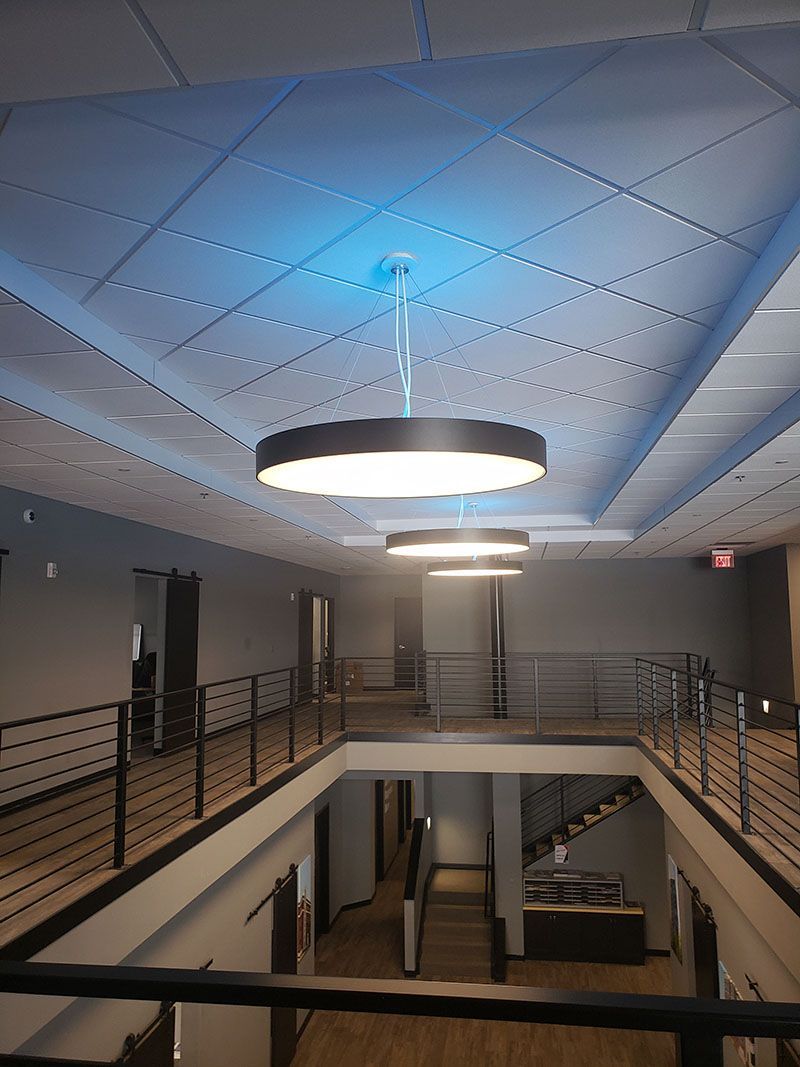 Two-story office hallway with modern lighting fixtures, metal railing, and a staircase.