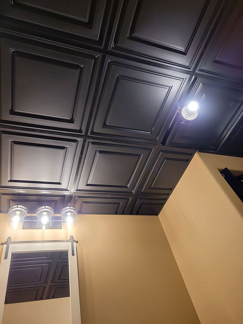 Black textured ceiling tiles with recessed lighting in a room with a light fixture and tan walls.