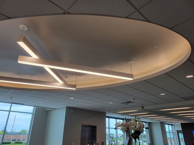 Modern interior with illuminated linear lights suspended from a curved ceiling. Large windows visible.