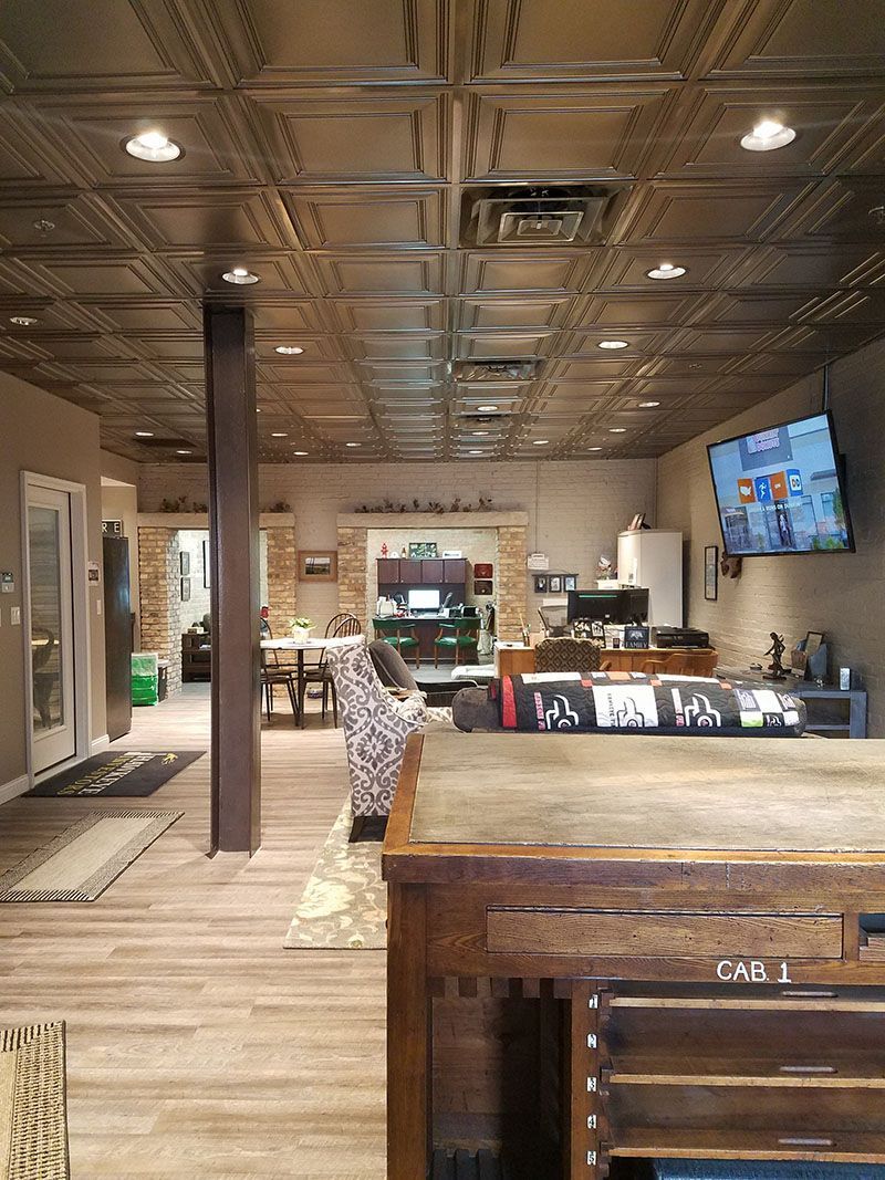 Interior shop with metal tile ceiling, hardwood floors, and a brown column. There is a television, display counter, and a doorway.