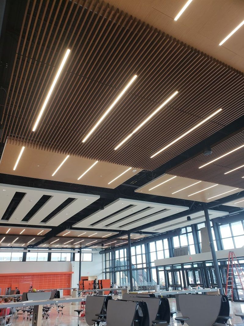 Wood and light-toned ceiling with linear LED lights. Restaurant interior with tables and windows visible.