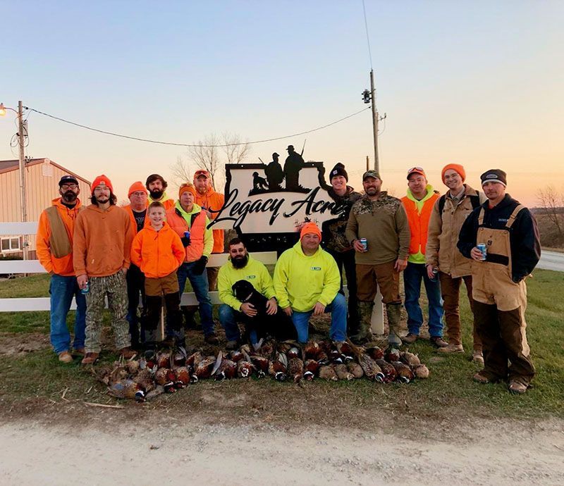 Group of people in hunting gear pose with dead pheasants in front of 