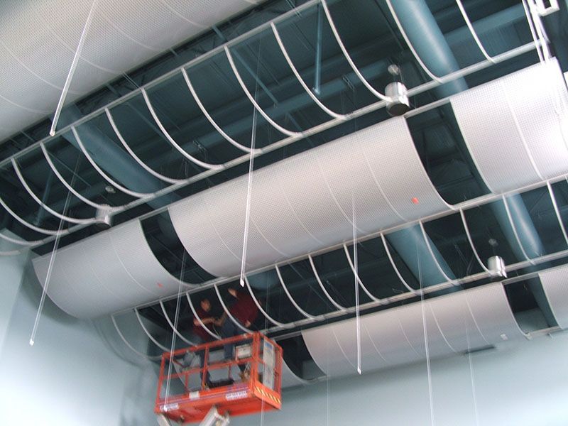 White cylindrical ceiling diffusers suspended from the ceiling with a lift in front of them.