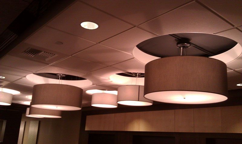 A row of drum-shaped pendant lights hanging from a white tile ceiling in a room.