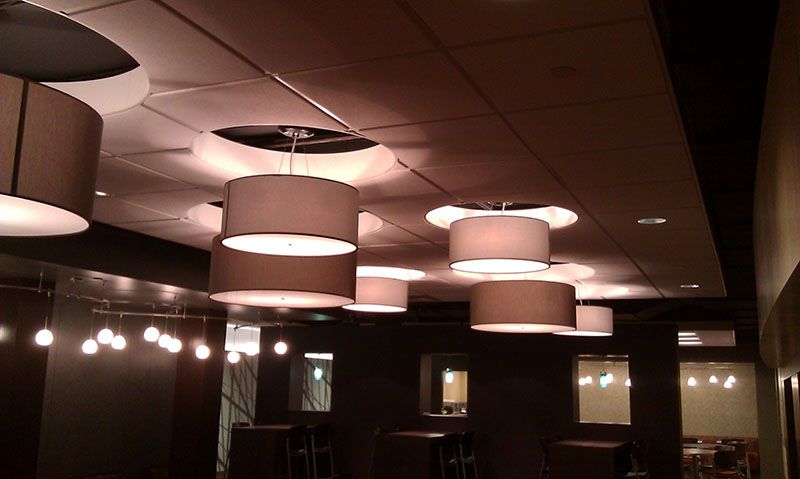 Restaurant interior with several drum pendant lights and wall sconces. Dark walls and ceiling with mirrors.