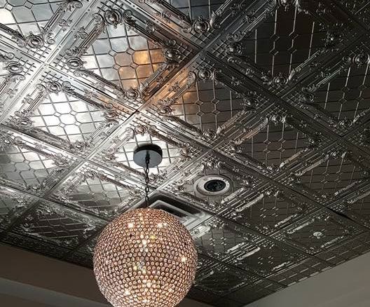 Ornate, silver-colored, patterned ceiling tiles with a hanging spherical light fixture.