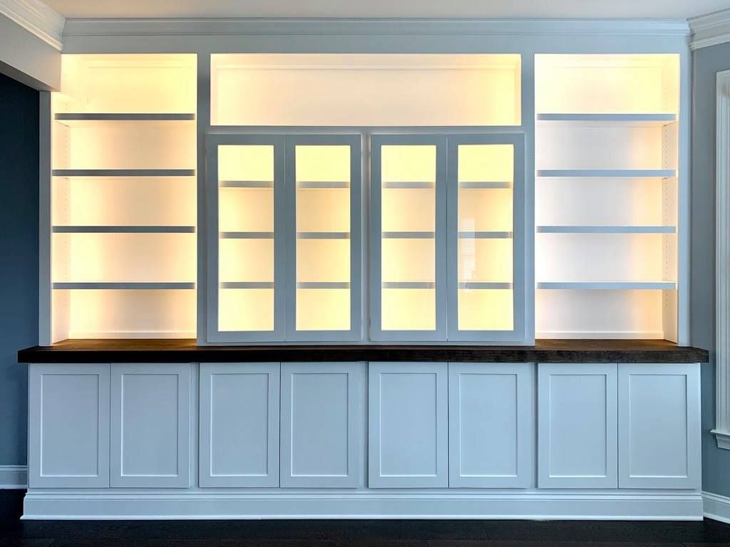 Built-in white cabinets with backlit shelves and glass doors in a modern room