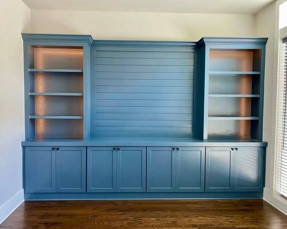 Blue built-in wall unit with shelves and cabinets in a room with hardwood floors.