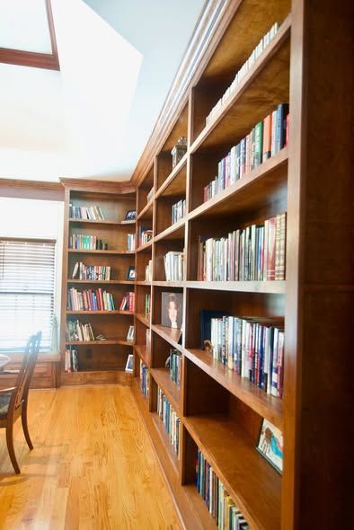 Tall wooden bookshelves filled with books in a brightly lit room with wooden floors and a window.