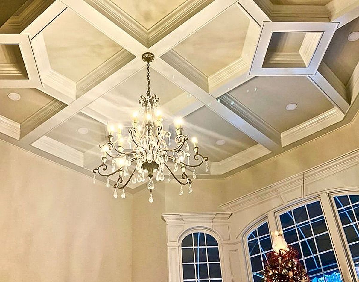 Ornate coffered ceiling with a chandelier above a bay window.