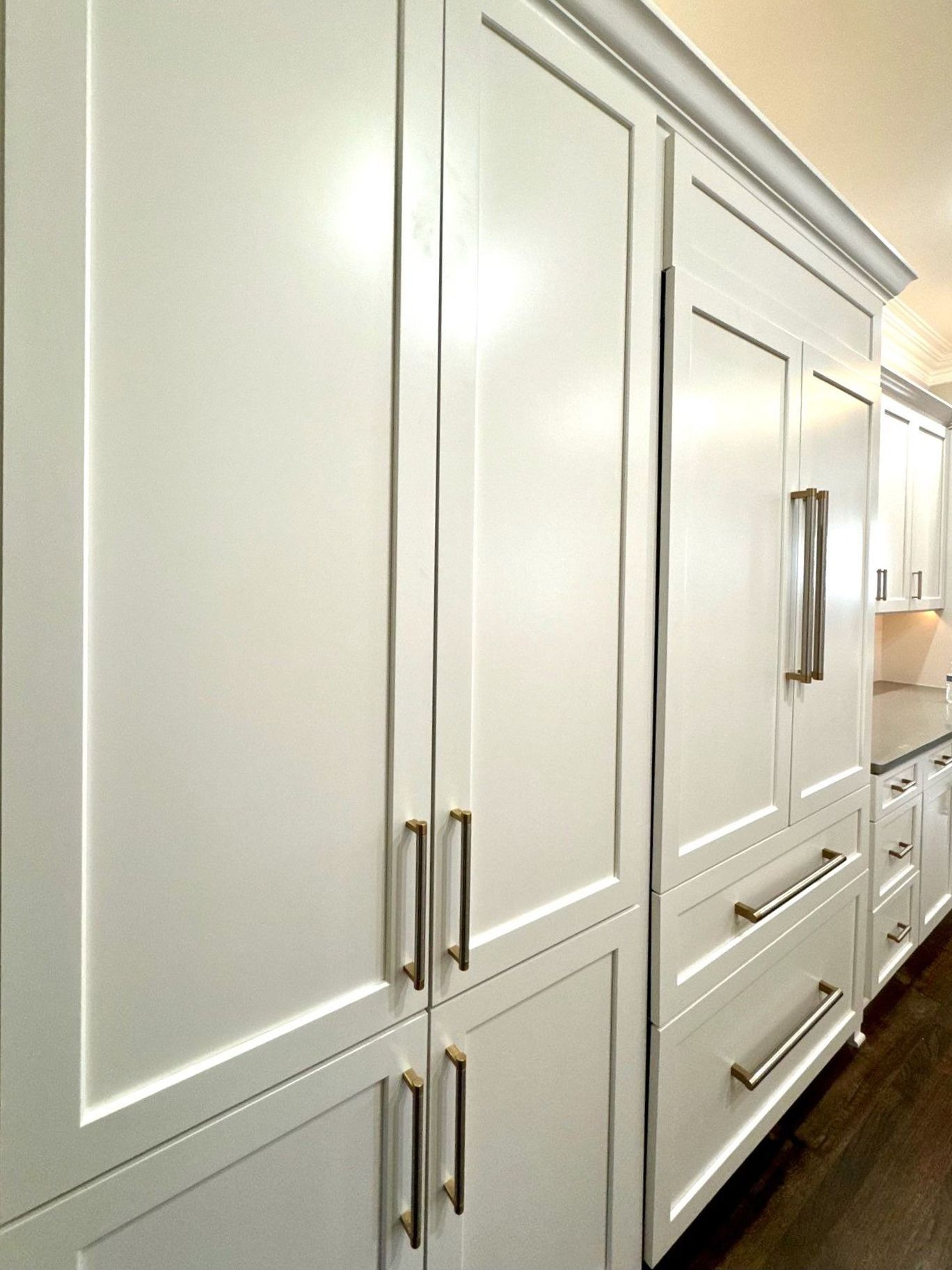 White paneled kitchen cabinets and a built-in refrigerator with metal handles in a modern home kitchen.