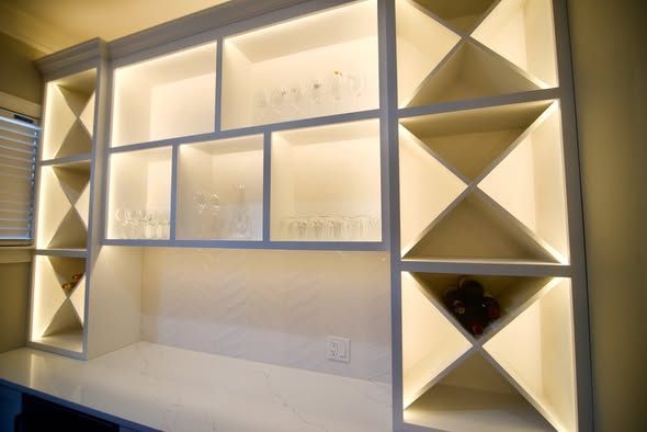 Built-in illuminated wall shelves with X-shaped side compartments and a white countertop against beige walls