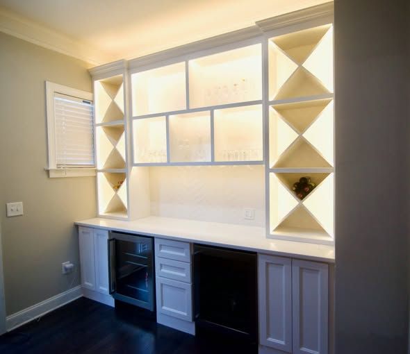 Built-in white home office desk with shelving, drawers, and cabinets beneath a window.