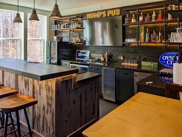 Modern pub interior with long bar, shelves of bottles, and stools by large windows