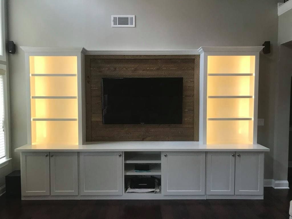 Built-in media wall with fireplace, TV, and lit display shelves above a white cabinet.