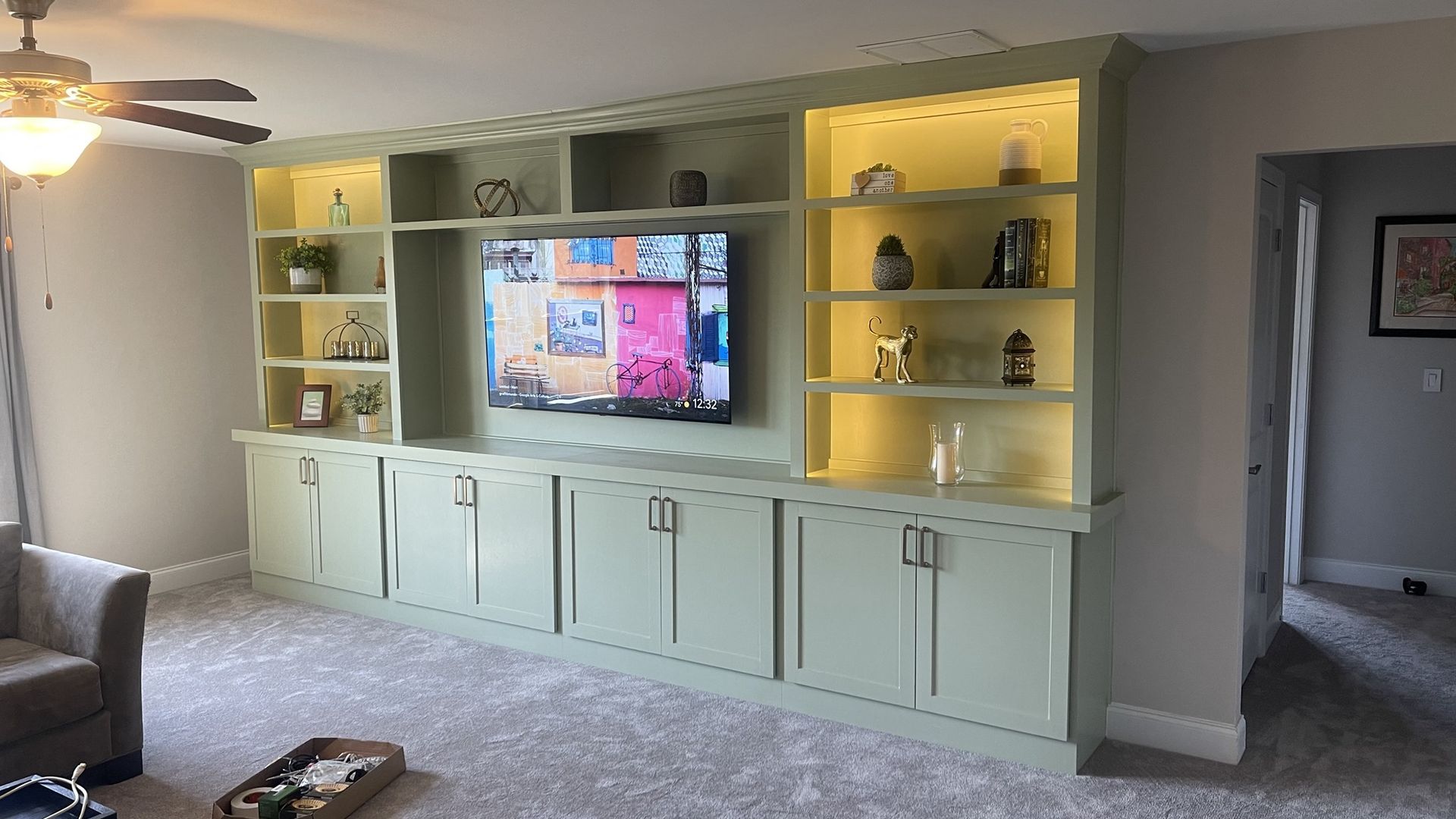 Living room wall with built-in shelving, a mounted TV, and light-colored cabinets under warm accent lighting