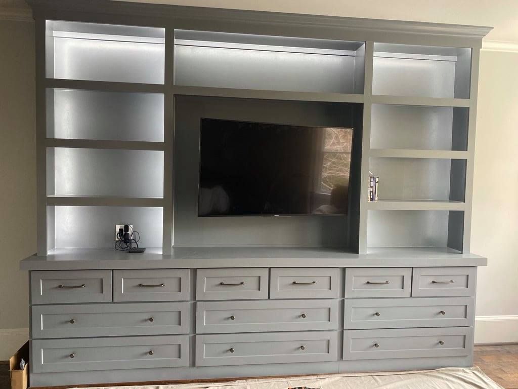 White built-in entertainment center with shelves, drawers, and a wall-mounted TV on a light wall.