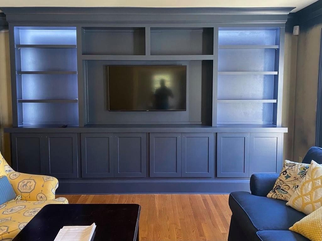 Modern living room with built-in entertainment center, TV, blue-gray cabinetry, and blue sofas with yellow pillows