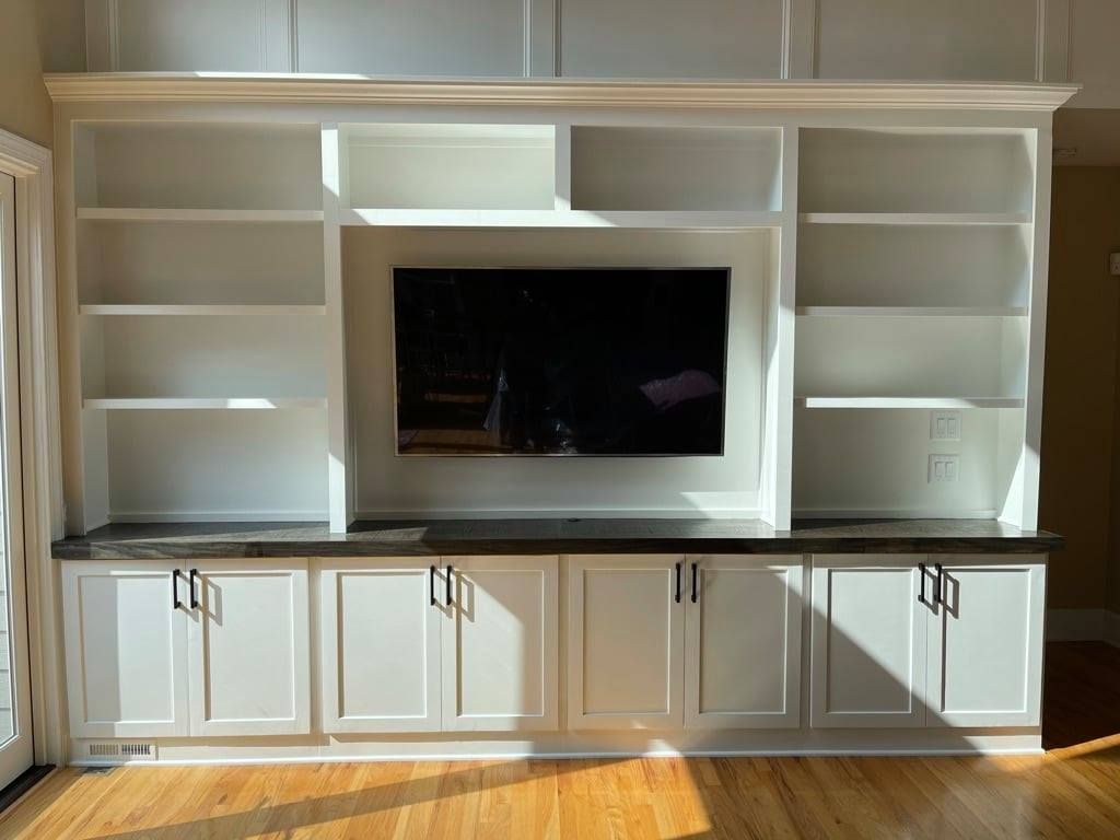 Built-in white entertainment center with shelves, cabinets, and a large TV in the middle