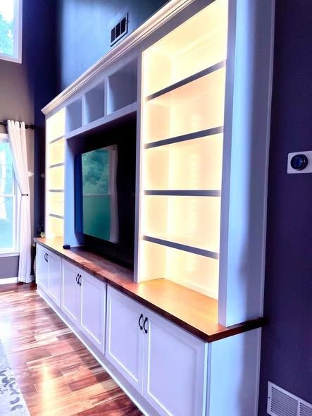 Built-in wall media unit with TV, white cabinets, and illuminated shelves along a hallway.
