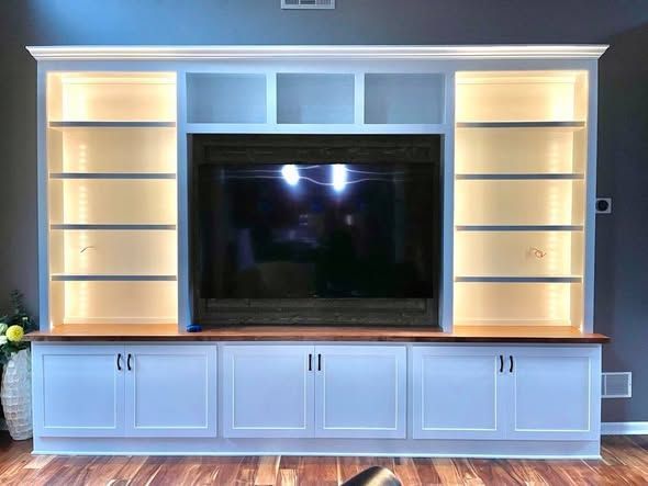 White built-in entertainment center with shelves, cabinets, and a large flat-screen TV in the middle